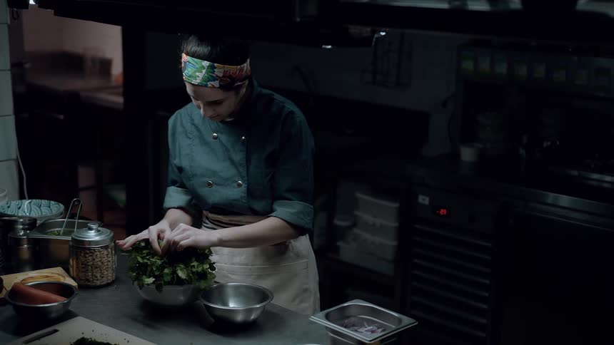 Chef picks through the greenery in a bowl while in the kitchen at night