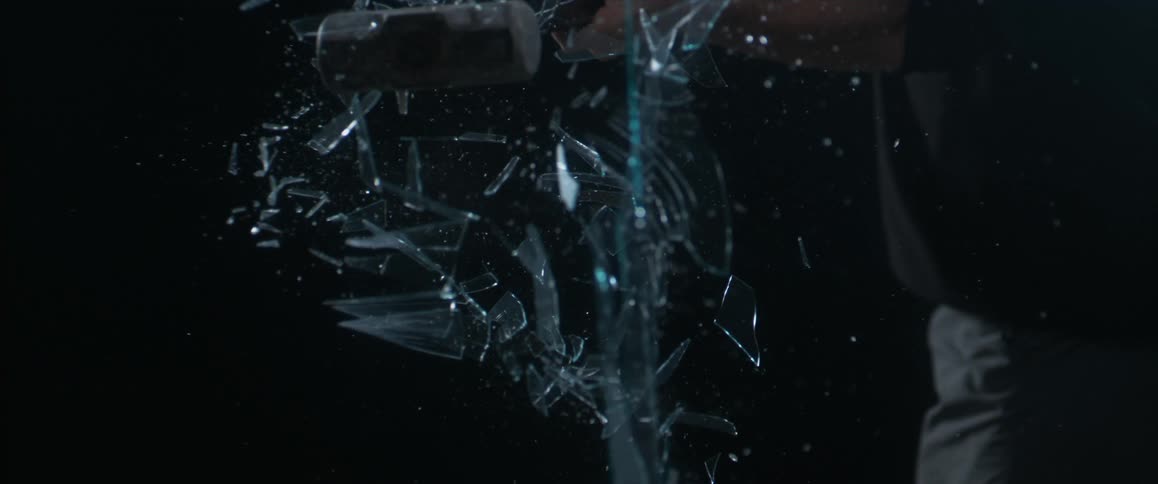 A man uses a long mallet to smash a piece of glass