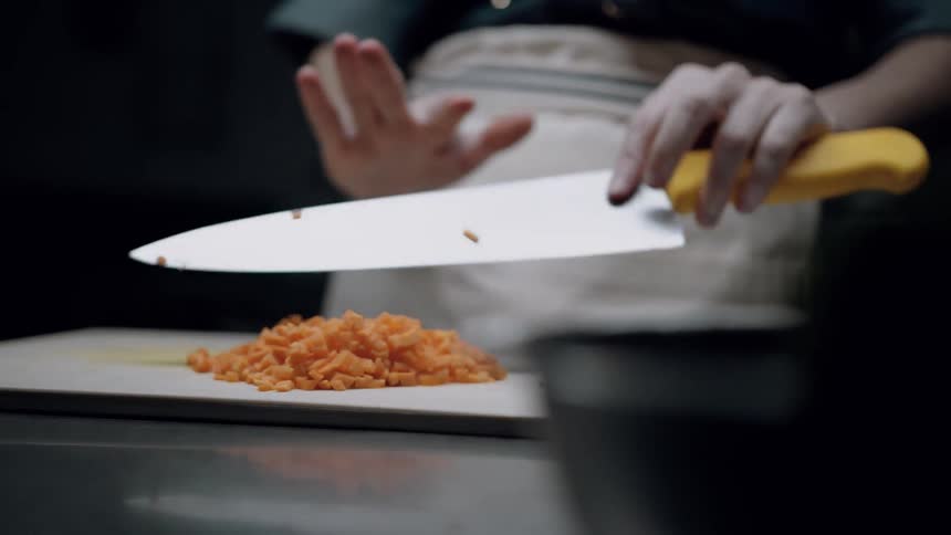 A chef slices carrots with a large knife on a chopping board