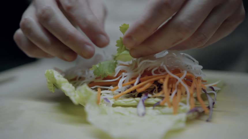 Hands carefully arrange a colorful medley of fresh vegetables including carrots noodles and cabbage onto a crisp lettuce leaf meticulously crafting a fresh food item