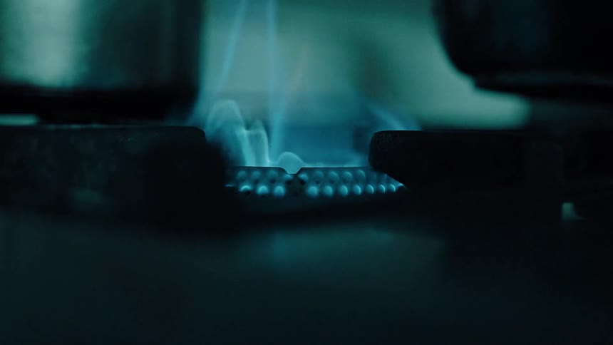 A blue gas flame burns beneath a pan placed on the flame heating it intensely on a stovetop