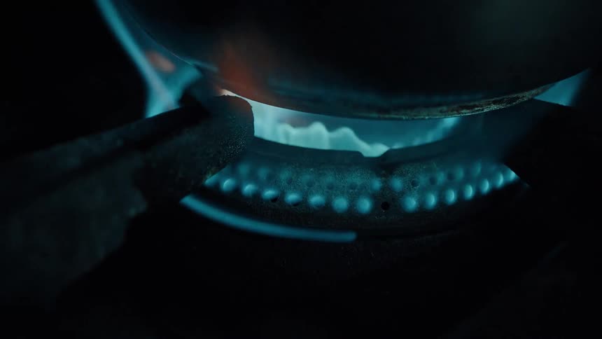 The video shows a closeup of a blue gas flame emanating from a burner with the bottom of a dark pan visible directly above it the flames flicker and dance around the base of the pan