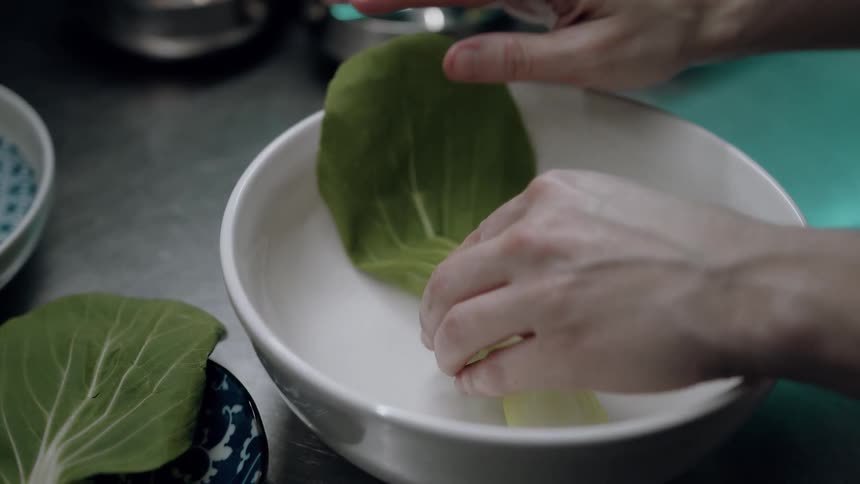 Close up of a woman arranging vegetable leaves in a white bowl