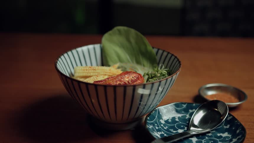 A bowl of food is served with vegetables