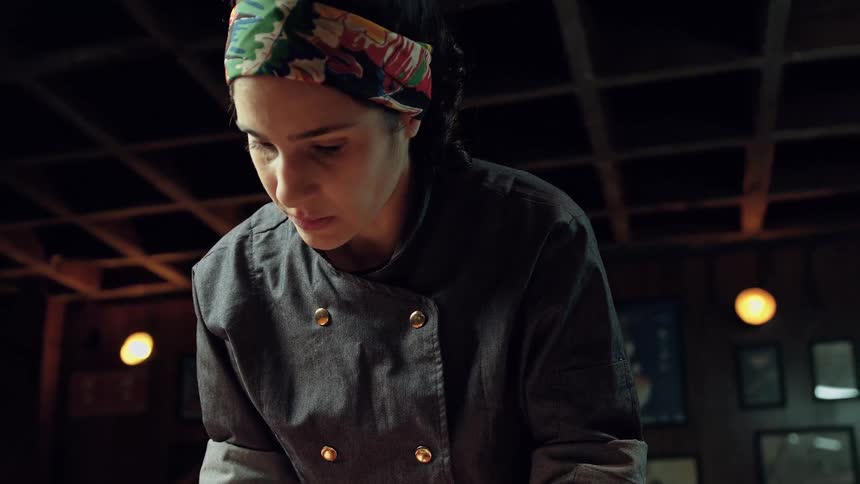 A focused chef in a dark uniform concentrates on her task under warm lighting