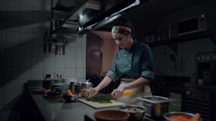A focused chef finely chops herbs in a stainlesssteel kitchen surrounded by prep bowls