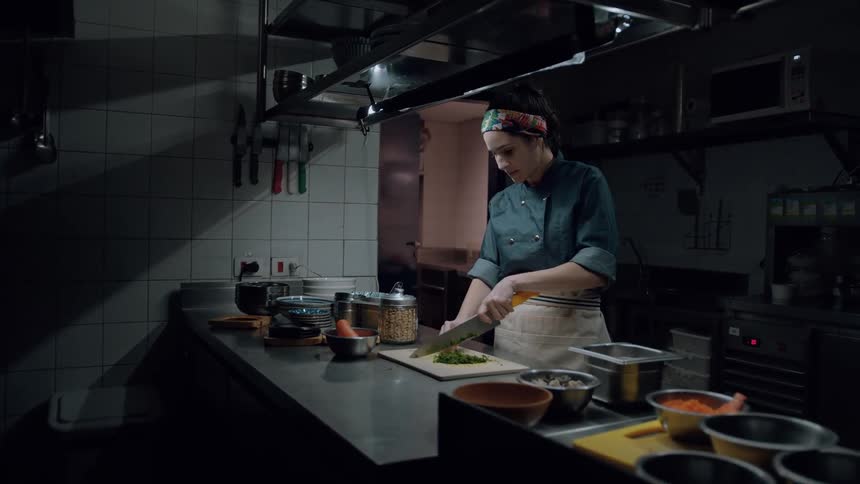 A female chef chops green vegetables in a restaurant kitchen