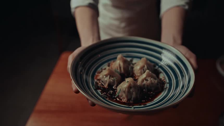 A chef serves a bowl of food presenting it on a table with a smile on her face