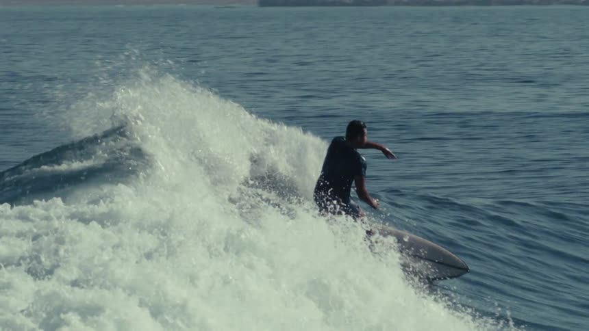 The video shows a surfer riding a wave the surfer dressed in a dark wetsuit is crouched low on the surfboard expertly navigating the foamy white water of the breaking wave