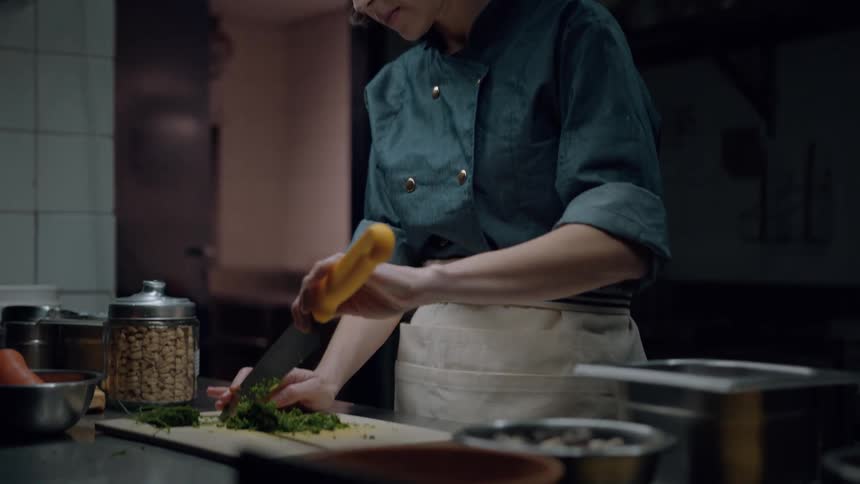 A chef chops herbs on a cutting board in a professional kitchen