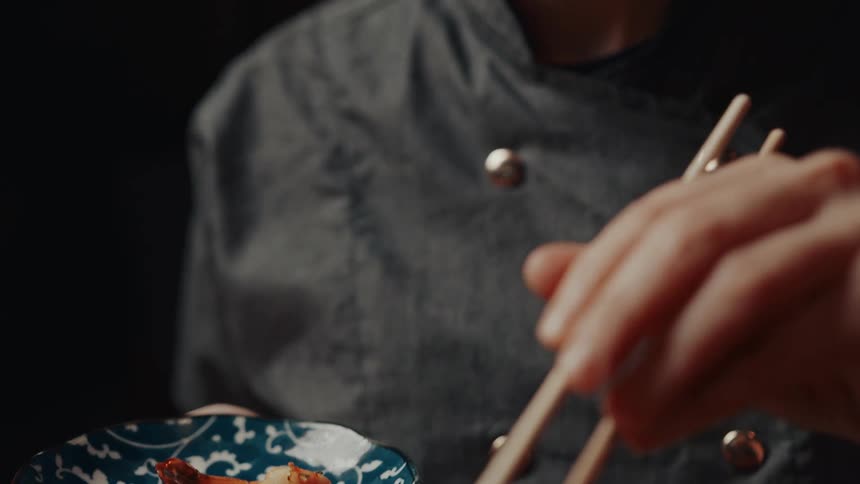 A woman using chopsticks to delicately pick up a fried shrimp from a bowl of what appears to be fried rice
