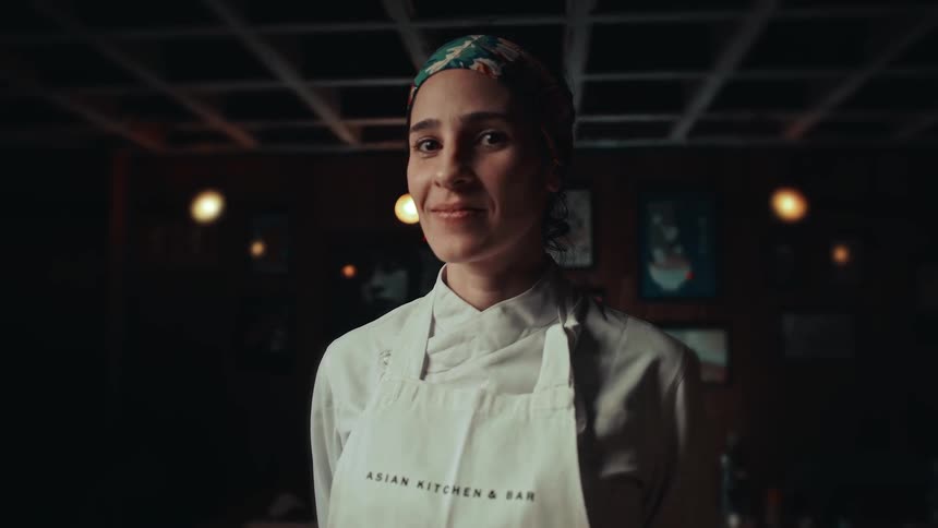 A chef stands in the kitchen wearing an apron smiling