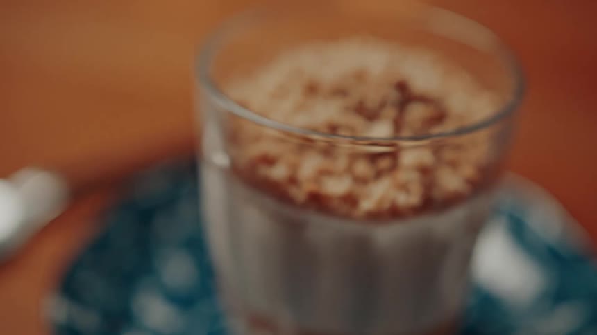 The video shows a glass filled with what appears to be a creamy dessert topped with a generous layer of crushed biscuits or nuts the focus shifts to show the texture and layers of the dessert in detail