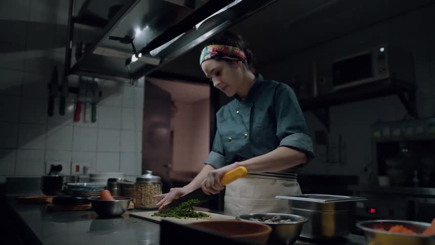 A young female chef chops vegetables with a knife on a chopping board while standing in the kitchen