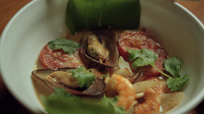Closeup of a bowl with mixed seafood and meat garnished with herbs