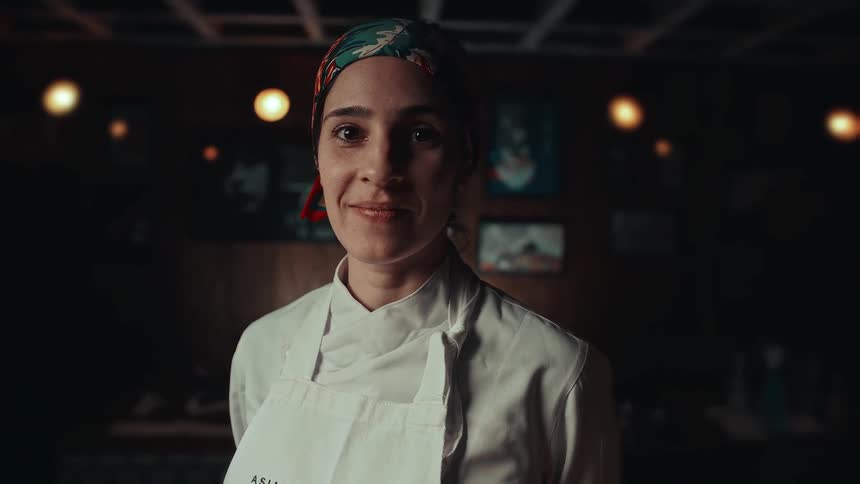 The chef is smiling as she stands in her restaurant