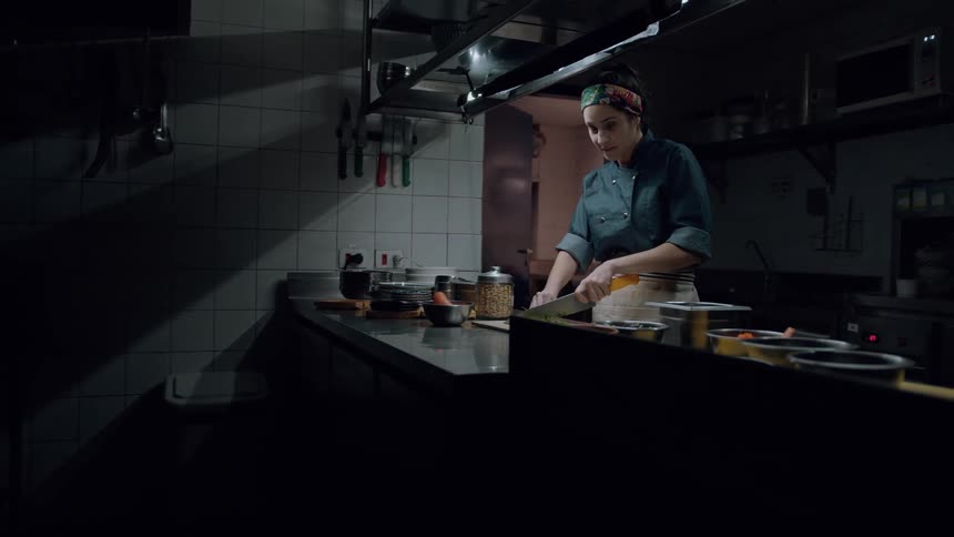 A young female chef cuts vegetables with a knife on a chopping board while standing in the kitchen