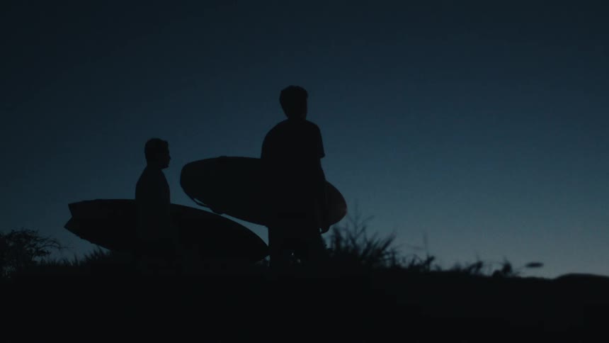 Two men stand on the hill holding surfboards