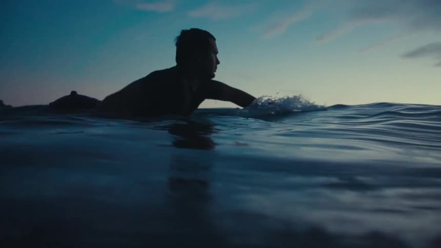 The surfer paddles out into the water on his board