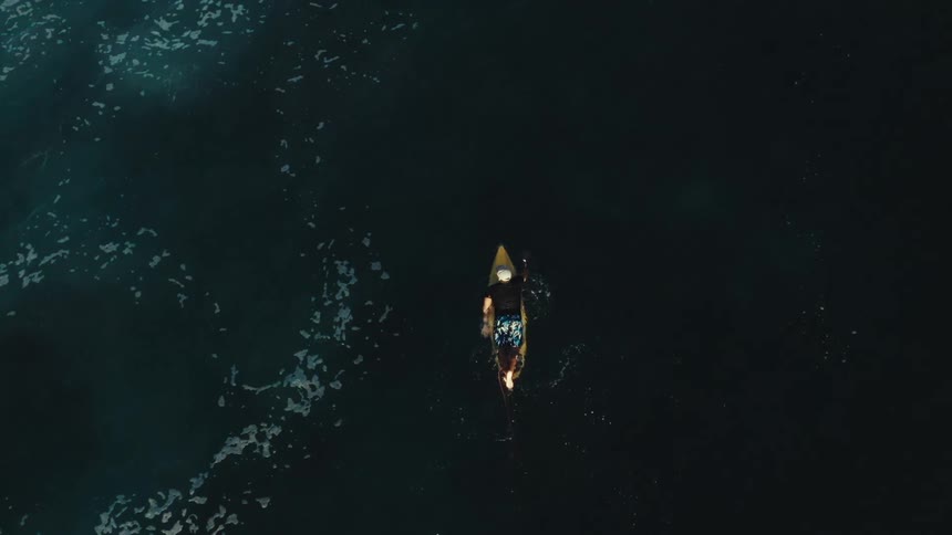 A lone kayaker paddles through dark still waters viewed from above