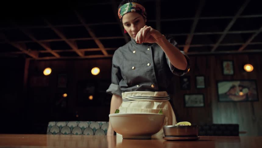 A chef seasoning a bowl of food in a restaurant setting
