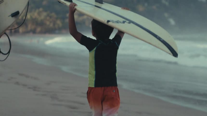 A surfer carries a surfboard while walking along the beach