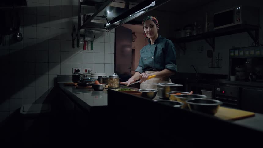 A woman chef cuts vegetables in the kitchen smiling