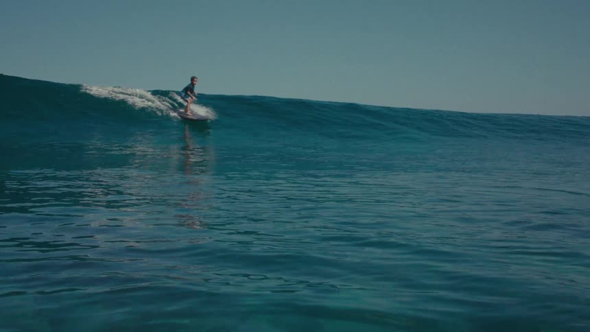 A man rides the long wave on his surfboard