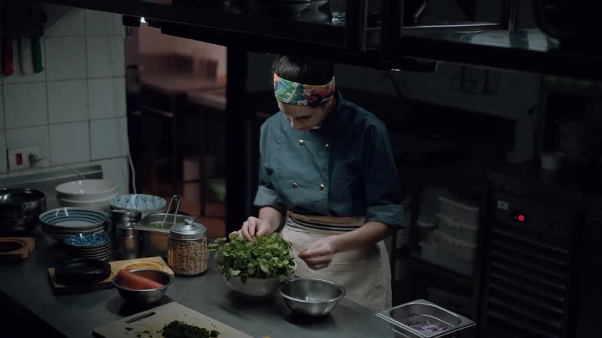 A female chef wearing a headband picks out vegetables in the kitchen