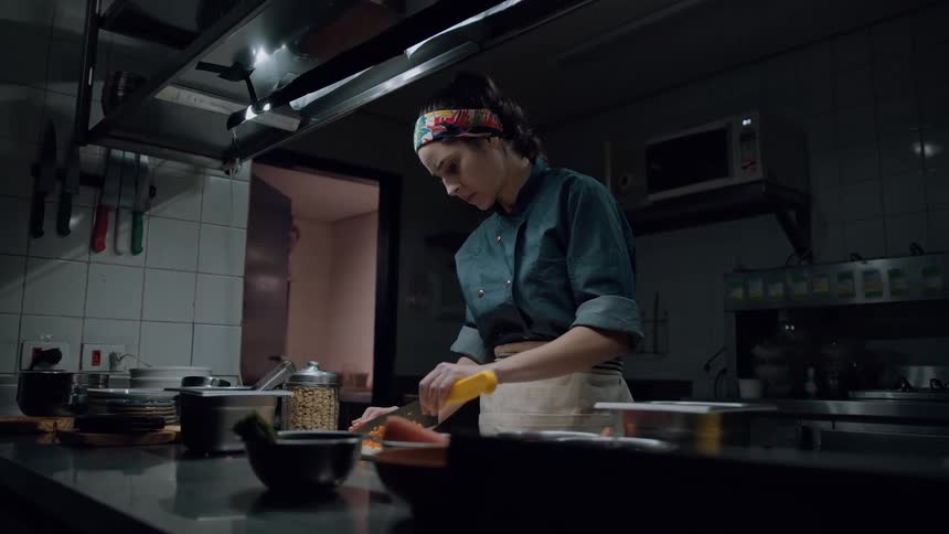 The woman is cutting carrots in the restaurant kitchen