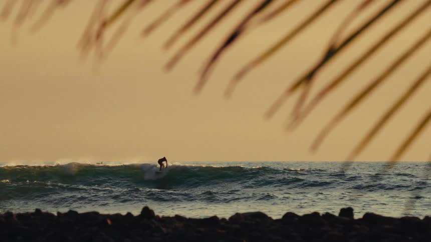 A young man surfs ocean waves close to the shore at sunset