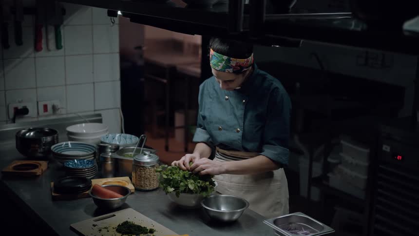 A young female chef picks vegetables in a bowl while standing in the kitchen