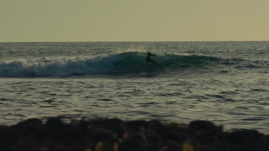 A man surfs an ocean wave toward the shore at sunset