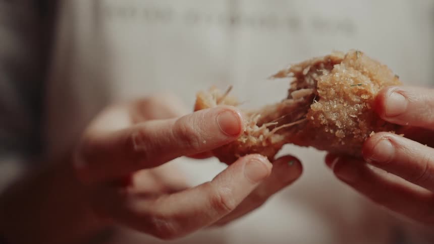 Hands gently pull apart a crispy golden croquette to reveal its savory filling