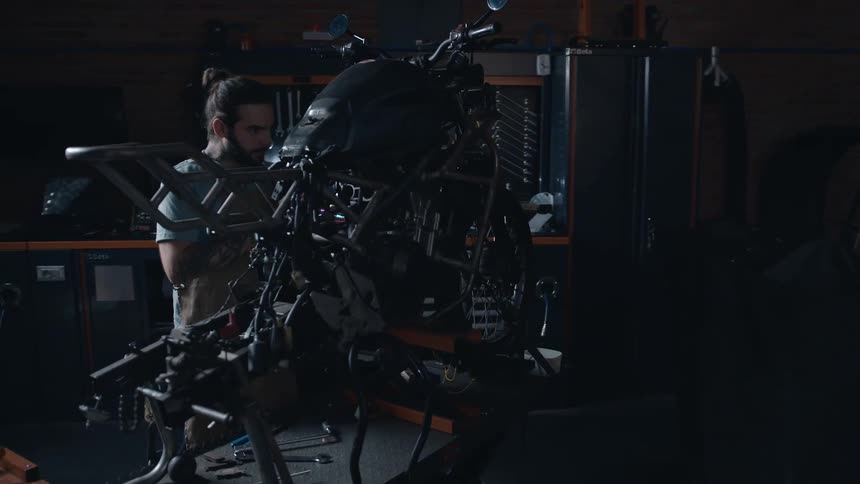 Mechanic working on a motorcycle wipes sweat off his forehead
