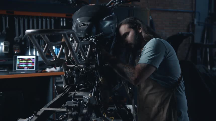 The mechanic works on the motorcycle and wipes his brow