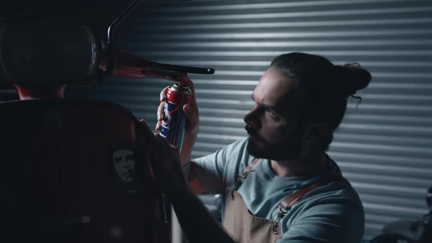 The mechanic is spraying lubricant on the moped