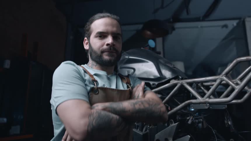 Close up portrait of a young male mechanic posing beside a motorcycle in a workshop
