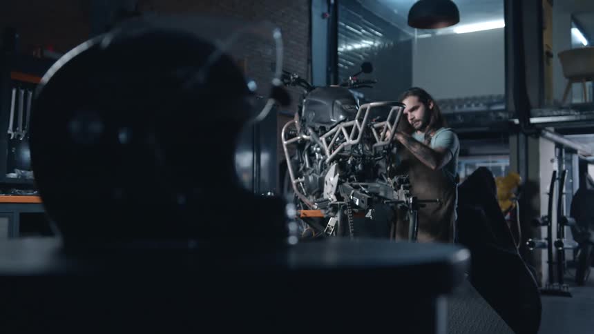 A mechanic works on a motorcycle in a dimly lit garage