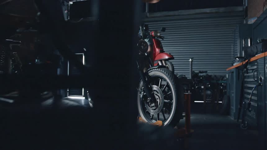 A man works on a custom motorcycle in a dimly lit garage surrounded by tools