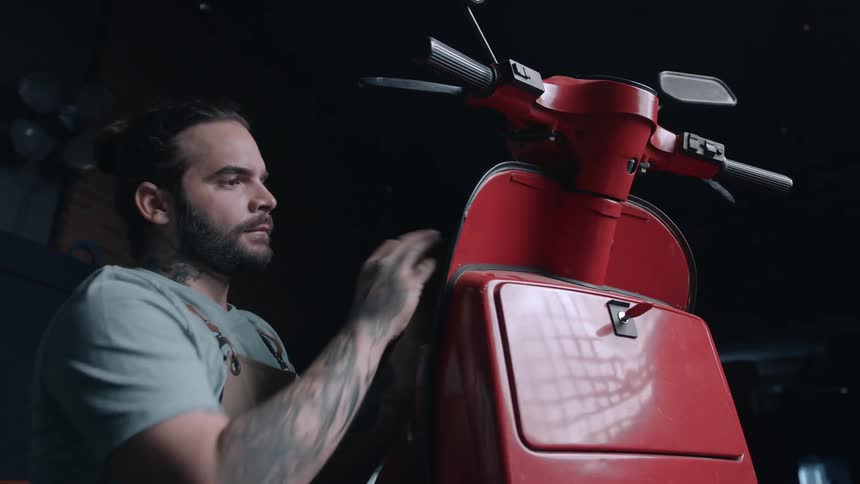 A mechanic cleans a red motorcycle with a cloth in a repair shop