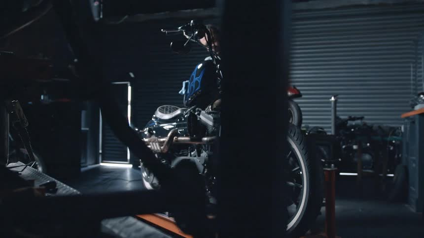 A young man wipes a motorcycle with a cloth in a workshop during daytime