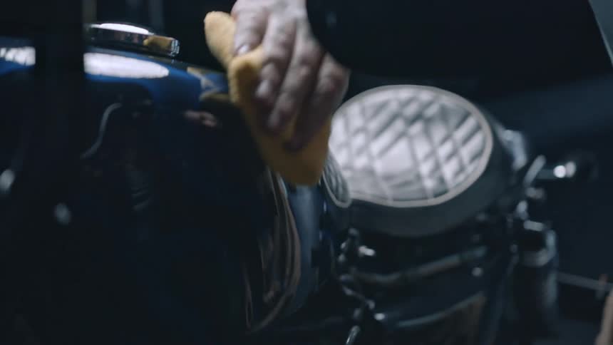 A man cleans a motorcycle with a rag inside a dealership