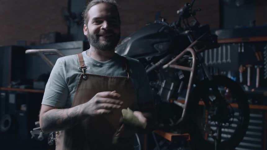 An auto mechanic is wiping his hands next to a motorcycle that is being repaired