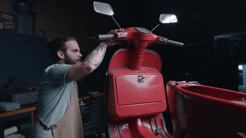 A mechanic works on a red scooter inside a mechanic workshop