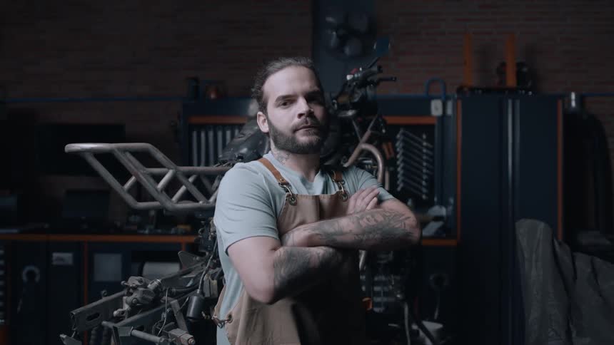 Mechanic in a brown apron crossing his arms inside a workshop
