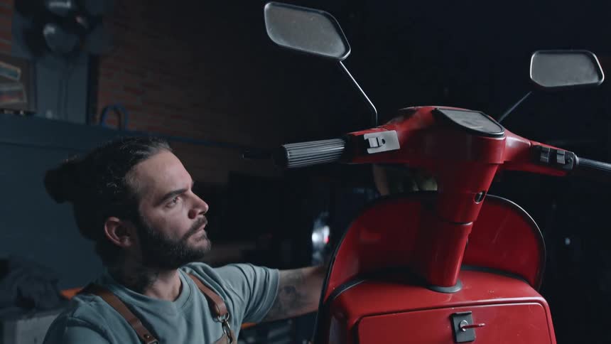 A mechanic cleans a red motorcycle with a cloth in a repair shop