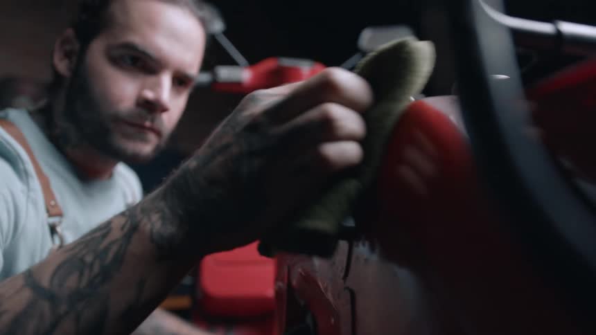 Man with a sponge cleaning the side of a red motorcycle