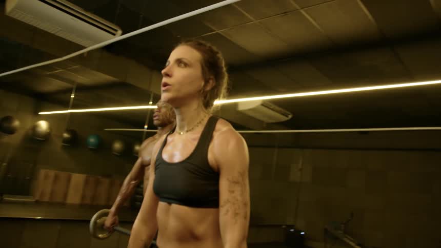 A man and a woman stand side by side in the gym lifting weights