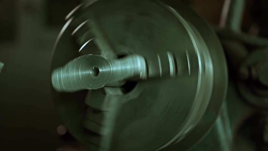 A closeup view of a metal lathe chuck as a hand reaches out to spin it manually